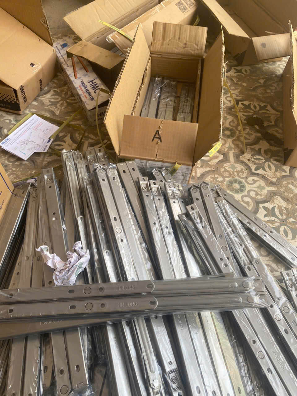 Thanh bản lề cửa Kin Long bằng inox xếp chồng cạnh thùng carton trên sàn